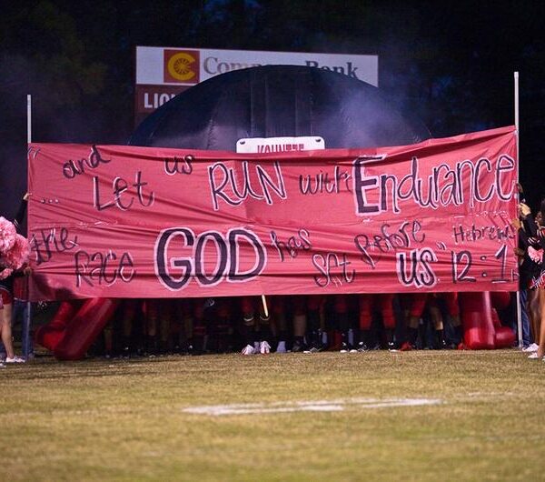 Cheerleaders holding banner with Bible verse