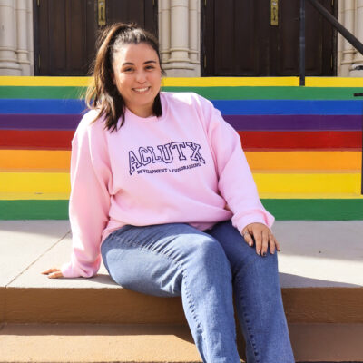 Image of Michele in a ponytail and wearing a pink sweatshirt that says ACLU of Texas.