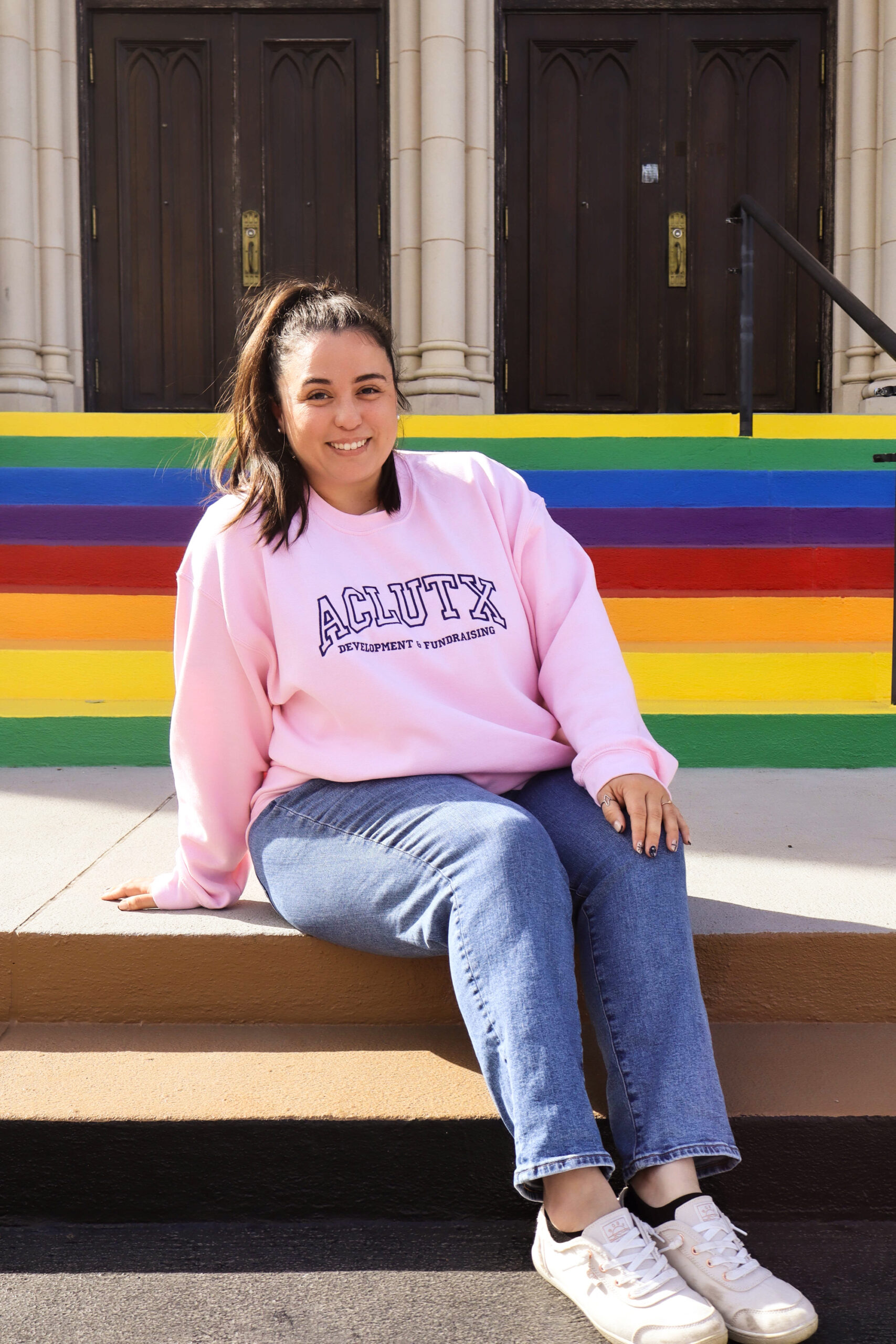 Image of Michele in a ponytail and wearing a pink sweatshirt that says ACLU of Texas.