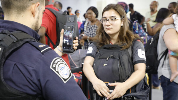 a young woman in line at the airport has her face scanned by a U.S. customs and border protection agent