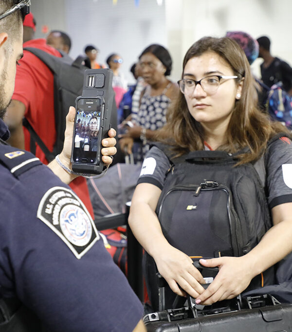 a young woman in line at the airport has her face scanned by a U.S. customs and border protection agent