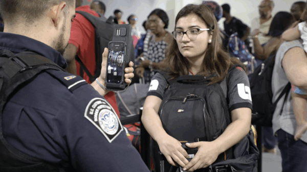 CBP agent scanning the face of a young woman using his smart phone