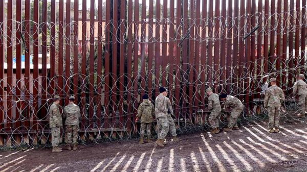 US military members are seen next to a red metal and barbed wire fence at the US border