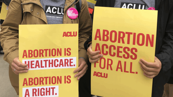 Two people are holding rally signs in support of reproductive freedom. On the left is someone holding a poster that reads "Abotion is healthcare. Aboriton is a right." On the right, a person holds a sign that reads "Abortino Access for All."