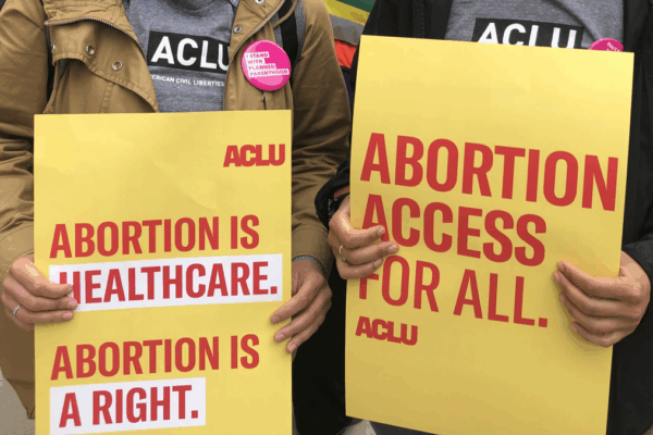 Two people are holding rally signs in support of reproductive freedom. On the left is someone holding a poster that reads "Abotion is healthcare. Aboriton is a right." On the right, a person holds a sign that reads "Abortino Access for All."