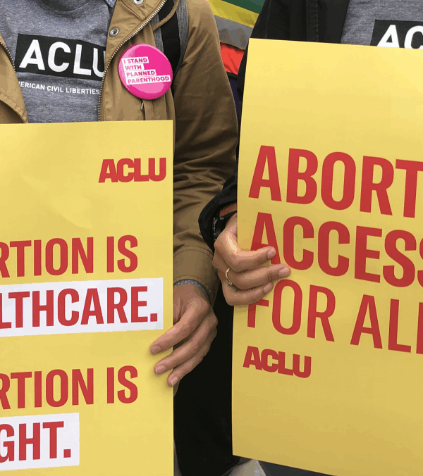 Two people are holding rally signs in support of reproductive freedom. On the left is someone holding a poster that reads "Abotion is healthcare. Aboriton is a right." On the right, a person holds a sign that reads "Abortino Access for All."