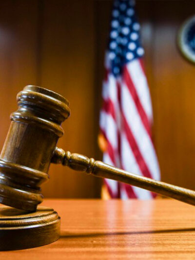 A gavel rests on the judge’s bench in a courtroom with American flag in the background.
