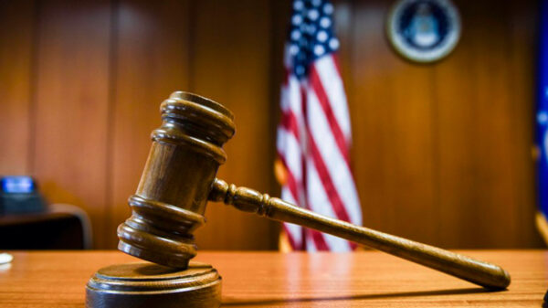 A gavel rests on the judge’s bench in a courtroom with American flag in the background.