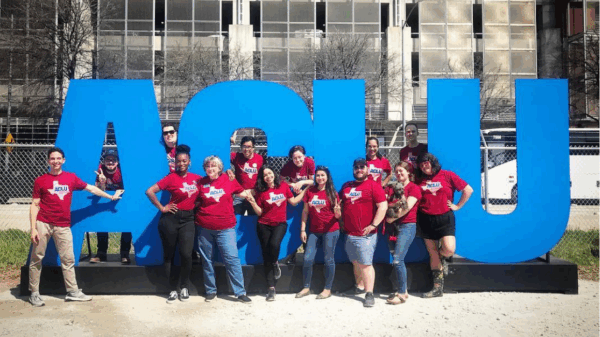 ACLU of TX staff stand in front of larger-than-life letters propped up outdoors.