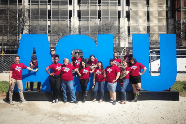 ACLU of TX staff stand in front of larger-than-life letters propped up outdoors.
