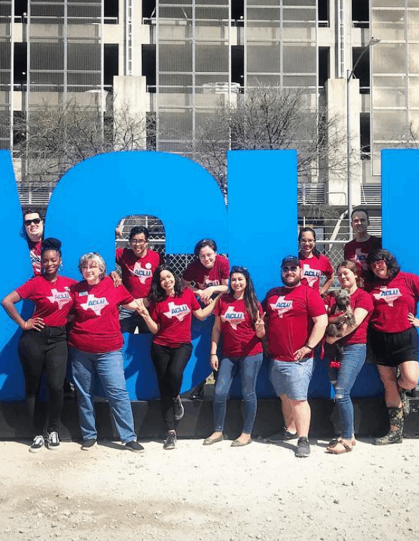 ACLU of TX staff stand in front of larger-than-life letters propped up outdoors.