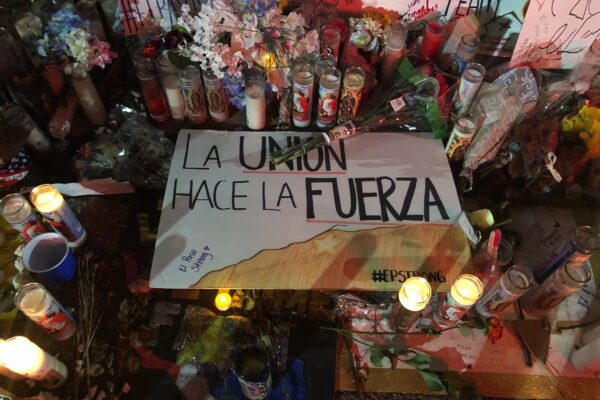 Photo: Handwritten signs, candles, and flowers adorn a section of a street. Pictured at center is a sign that says "La union hace la fuerza."