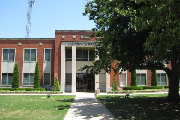 Photo: A tree in the foreground obscures a portion of a brick administration building in the background