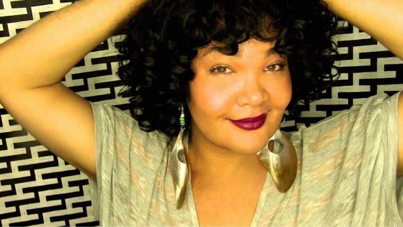 Photo: Diamond Stylz raises her arms to her head as she poses for a photo in front of a patterned background