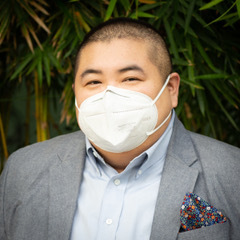 Photo: Emmett Schelling poses for a photo in front of some foliage outside. He wears a mask.