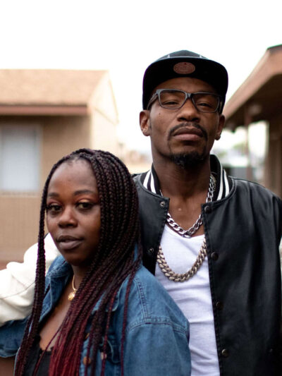 A young Black couple stand side by side on a balcony posing for the camera