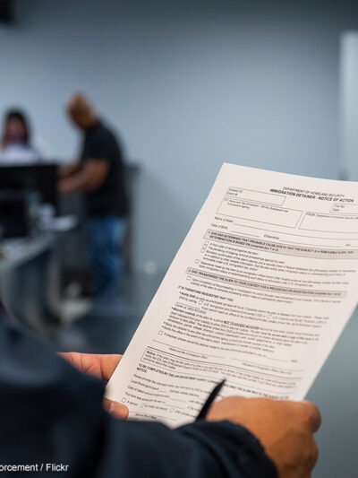 An ICE agent holding an Immigration Detainer form.