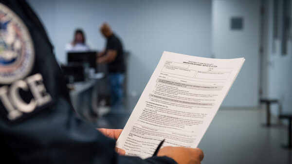 An ICE agent holding an Immigration Detainer form.