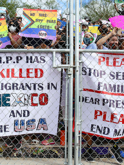 People press signs against a closed gate to the migrant encampment, asking then President Donald Trump to end the Migrant Protection Protocols during a rally at the encampment in Matamoros, Tamaulipas, Mexico on October 25, 2020.