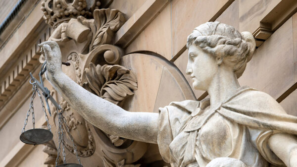 A statue of the goddess Justitia holds a pan of scales in front of the building of the district and regional court.