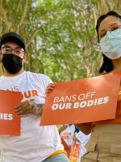 Two people holding signs that say Bans off our bodies