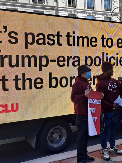 Demonstrators standing in front of a mobile billboard that says, “It’s past time to end Trump-era policies at the border.”