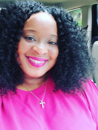Smiling woman with black curly hair wearing a pink shirt