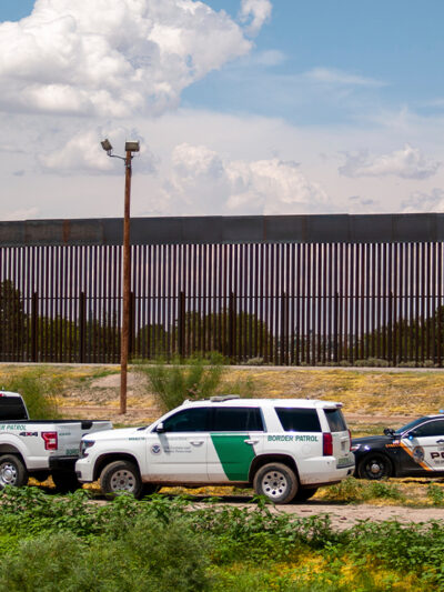 U.S. Border patrol vehicles converge with local police car by border fence.