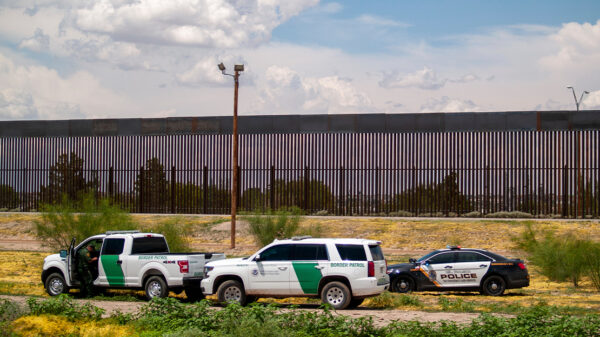 U.S. Border patrol vehicles converge with local police car by border fence.