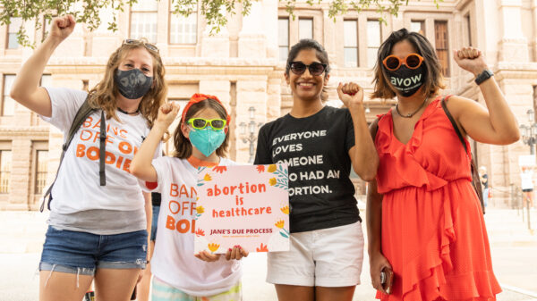 an image of four people with their fists up holding a sign that says abortion is healthcare