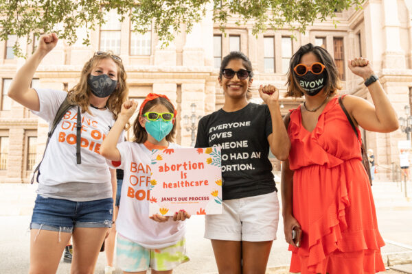 an image of four people with their fists up holding a sign that says abortion is healthcare