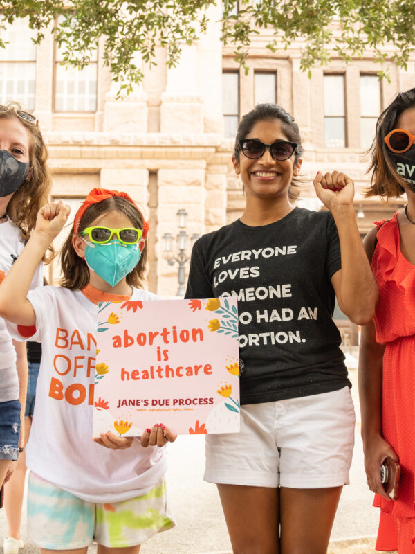 an image of four people with their fists up holding a sign that says abortion is healthcare