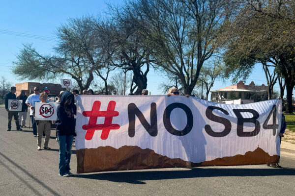 Protesters carry a banner that says NO SB 4.