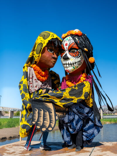 Two giant puppets embrace in the middle of the Rio Grande