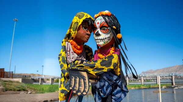 Two giant puppets embrace in the middle of the Rio Grande