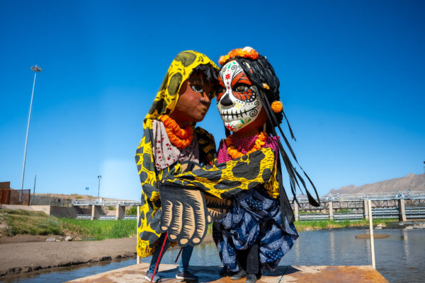 Two giant puppets embrace in the middle of the Rio Grande
