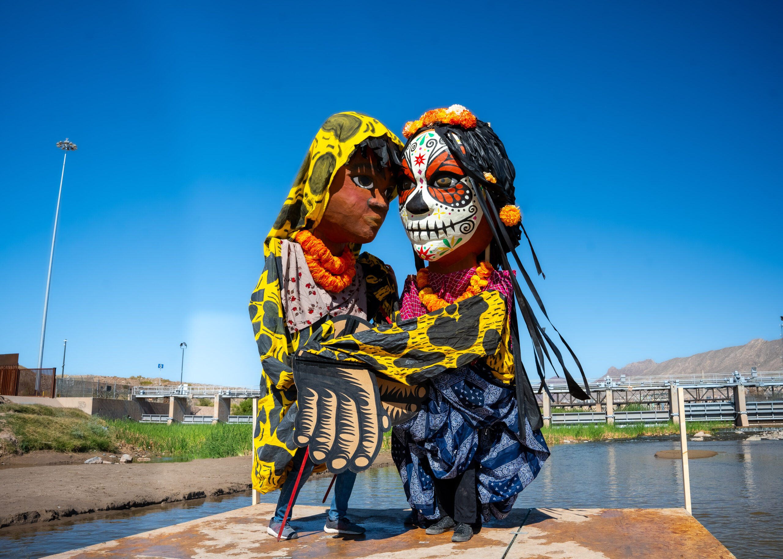 Two giant puppets embrace in the middle of the Rio Grande