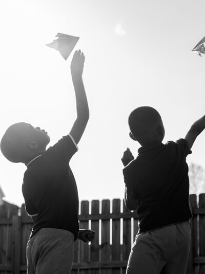 As the sun is shining, two children fly paper airplanes.