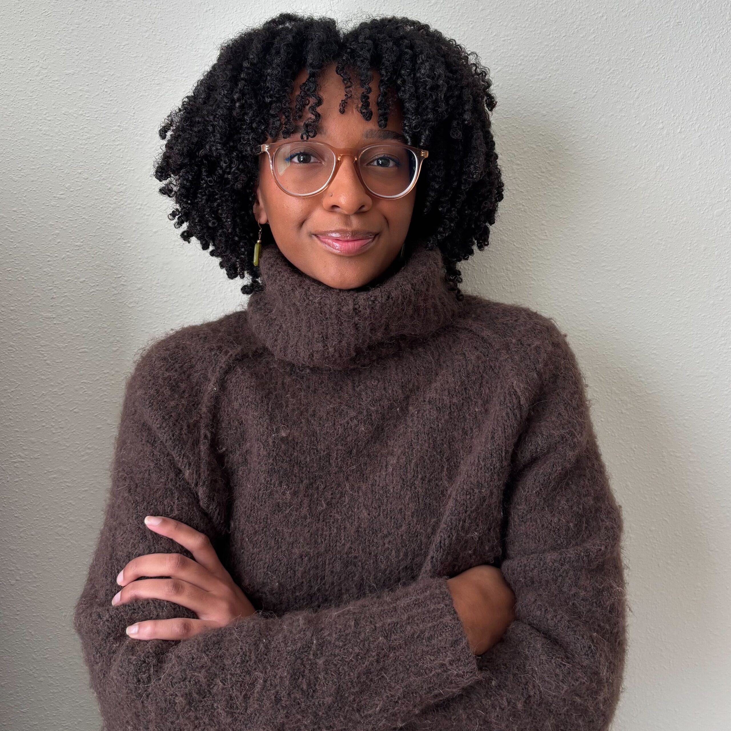 Image of Ayania in a brown turtleneck sweater with their arms crossed.