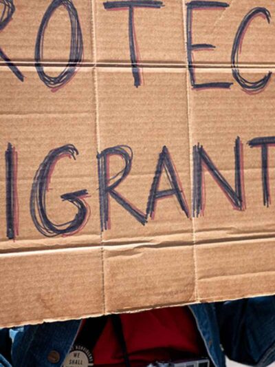Photo of a cardboard protest sign that reads "PROTECT MIGRANTS" in all caps.