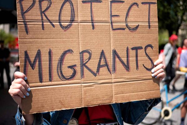 Photo of a cardboard protest sign that reads "PROTECT MIGRANTS" in all caps.