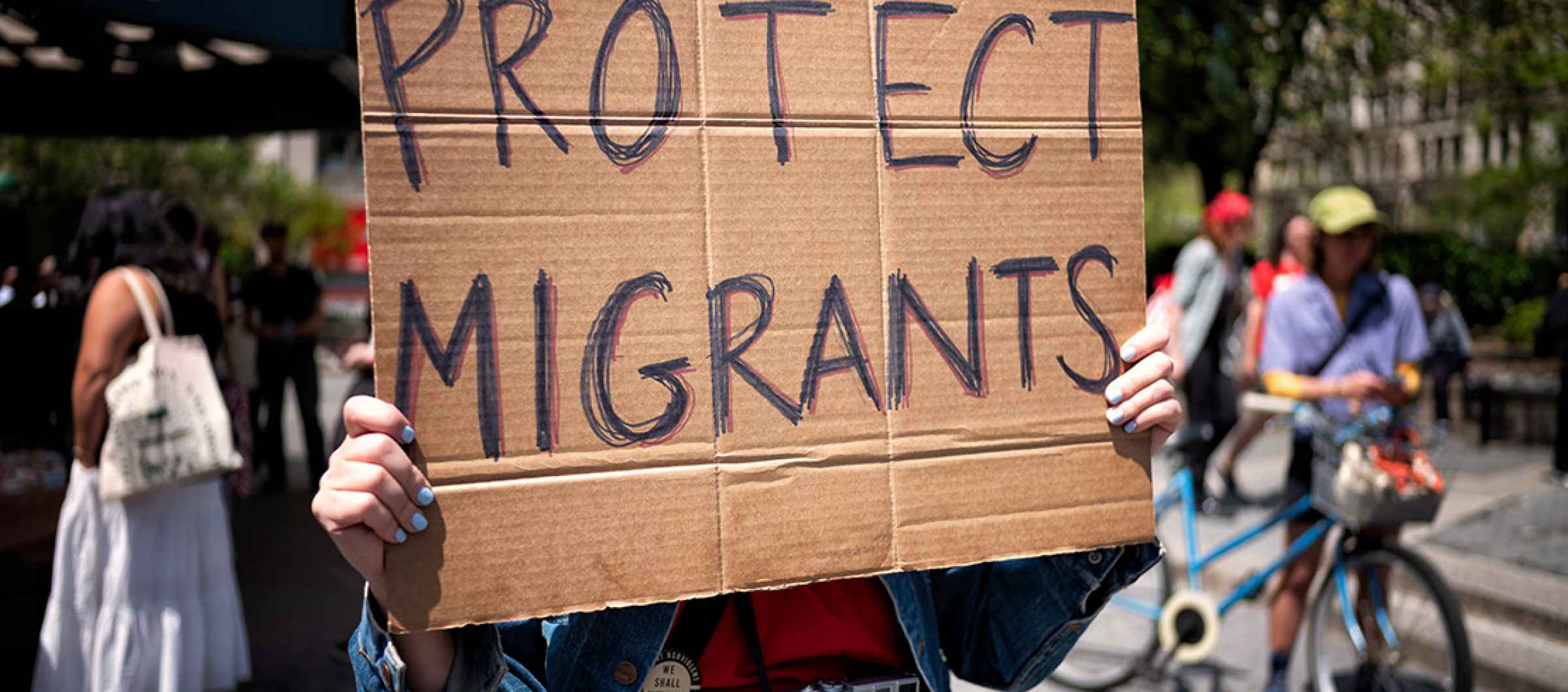 Photo of a cardboard protest sign that reads "PROTECT MIGRANTS" in all caps.