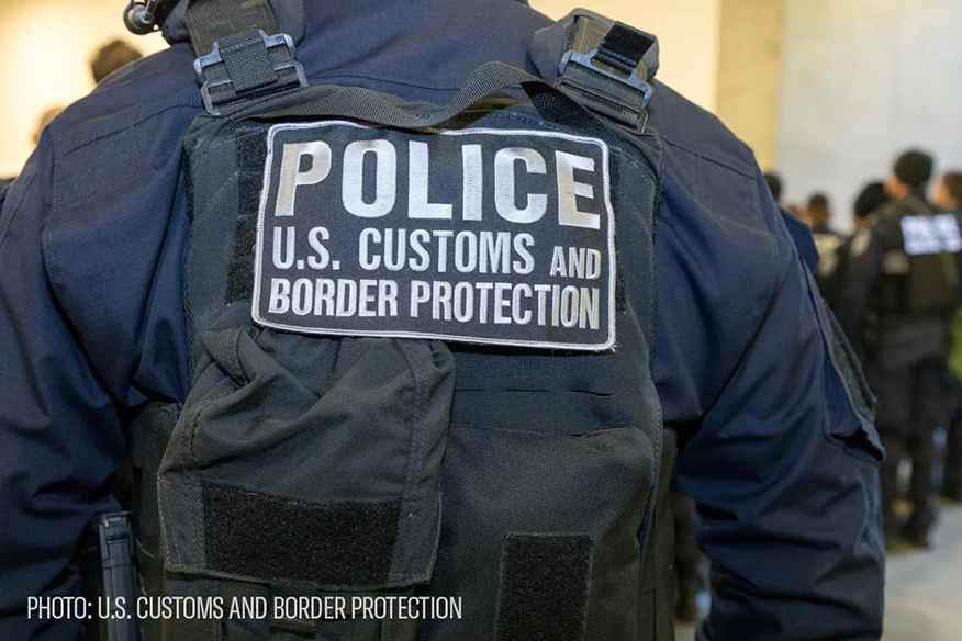 image of an ice agent from behind with his vest reading POLICE U.S. CUSTOMS AN BORDER PROTECTION