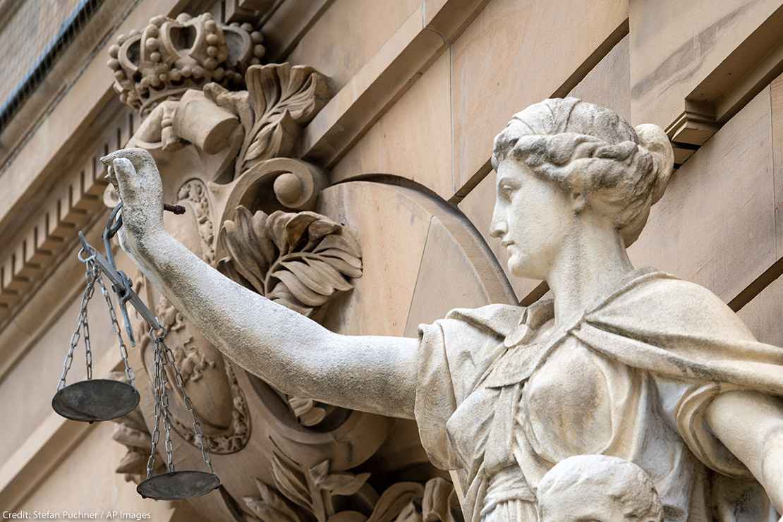 A statue of the goddess Justitia holds a pan of scales in front of the building of the district and regional court.