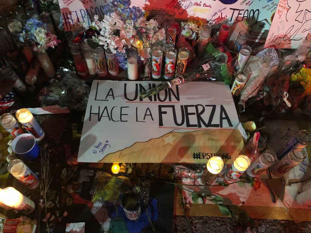 Photo: Handwritten signs, candles, and flowers adorn a section of a street. Pictured at center is a sign that says "La union hace la fuerza." 
