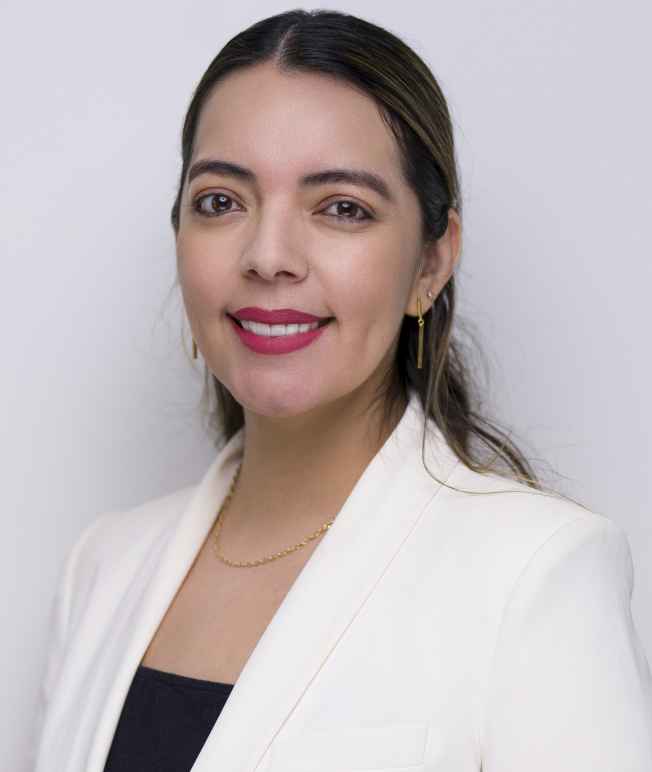 Image: A photo shows Cristina Soto posing for the camera in front of a solid background.