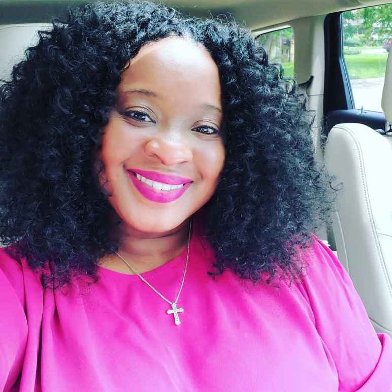 Smiling woman with black curly hair wearing a pink shirt