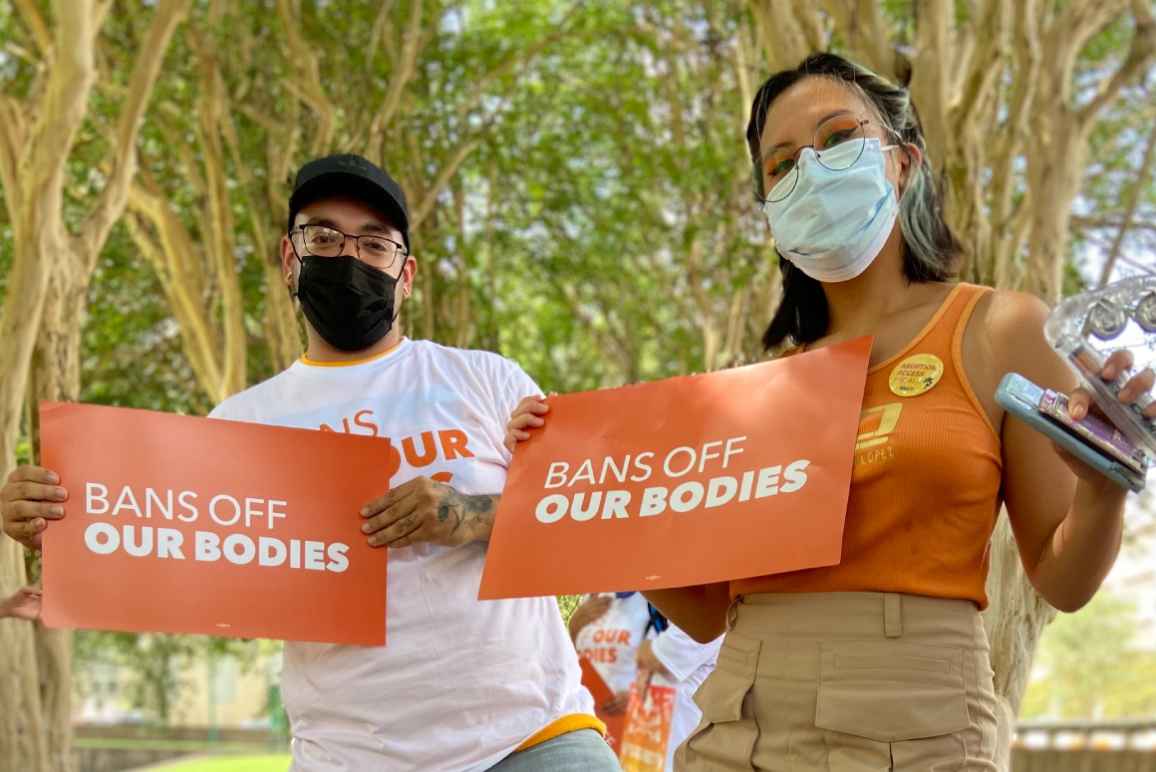 Two people holding signs that say Bans off our bodies