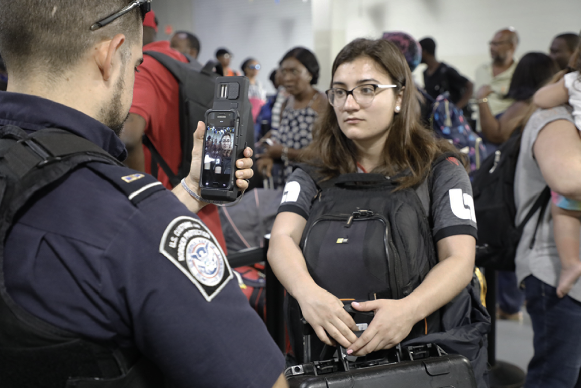 CBP agent scanning the face of a young woman using his smart phone