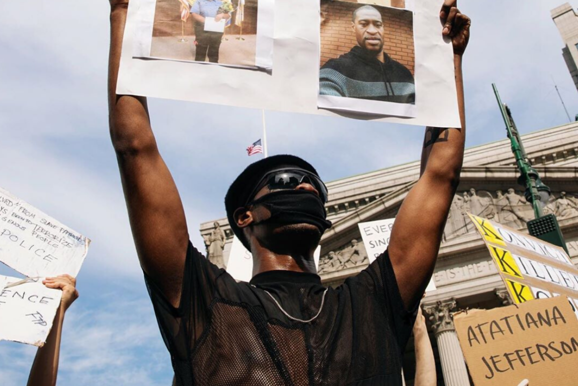 Photograph of black man protesting holding a George Floyd poster above his head